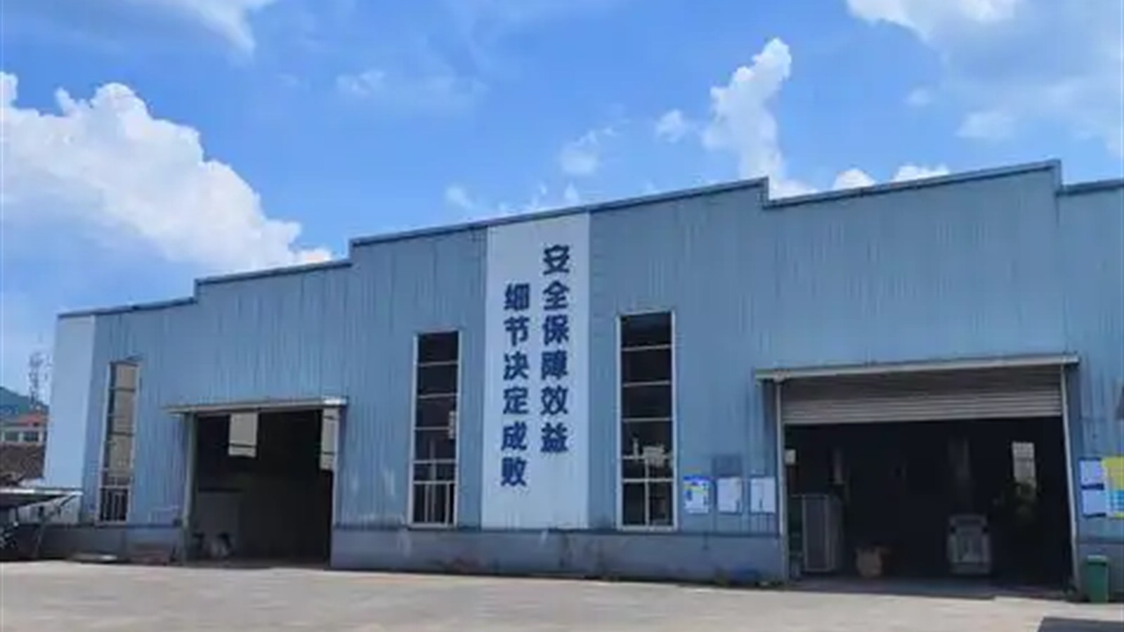 蓝天下的机械加工厂房外景，厂房墙面可见安全生产标语